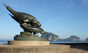 Bronze dugong statue on a round stone pedestal beside the sea, with limestone karst islands on the horizon