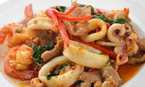 Close-up of Thai stir-fried seafood with squid rings, shrimp, pork, holy basil and red chilli on a white plate