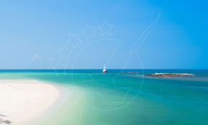 White sand beach with turquoise shallow water, a small white sailboat and rocky islet under clear blue sky