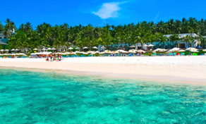 Tropical white-sand beach lined with colourful umbrellas and palm trees beside clear turquoise water