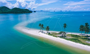 Aerial view of a curved sandy spit lined with palm trees jutting into turquoise sea, islands on horizon