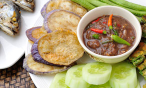 Thai nam prik chilli dip in a bowl with fried mackerel, eggplant slices, cucumber and long beans on a white plate