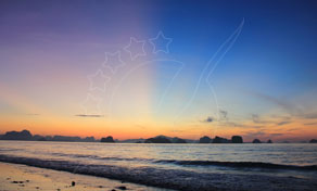 Sunset over a calm sea with limestone karst islands on the horizon and gentle waves on a sandy beach