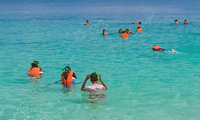 Snorkellers in orange life jackets floating in clear turquoise shallow sea on a sunny day