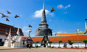 White Buddhist chedi with gilded spire at a Thai temple complex, pigeons in flight under blue sky