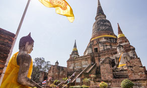 Ancient brick chedi at a Thai temple with seated Buddha statues in orange robes and a yellow flag