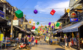 Busy Bangkok backpacker street lined with shops and hanging colourful cube decorations under a blue sky
