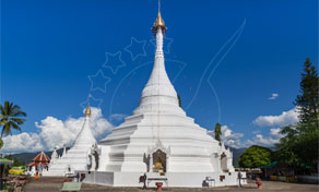 White Buddhist chedi with golden spire at a hilltop temple under blue sky, Mae Hong Son, Thailand