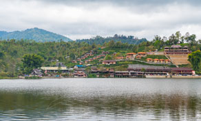 Hillside lakeside village of wooden buildings and resorts backed by forested mountains under overcast sky