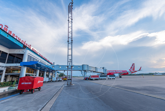 AirAsia aircraft parked on the apron at Surat Thani Airport terminal with jet bridge and baggage cart at dusk