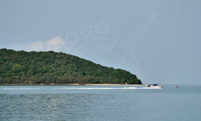 Speedboat leaving a white wake beside a forested tropical island under a hazy blue sky
