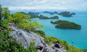 Panoramic viewpoint over turquoise sea and limestone islands from a rocky cliff framed by green foliage