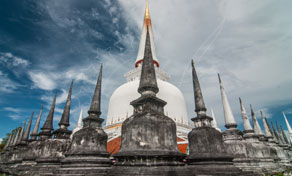 White chedi with golden spire surrounded by dark stone stupas at a Thai Buddhist temple under blue sky