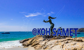 Bronze mermaid statue on rocks above turquoise sea at Koh Samet beach, with boats offshore under blue sky