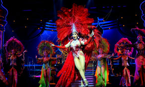 Cabaret performers in red feather headdresses and sequined costumes on a blue-lit stage during a live show