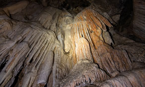 Warm-lit flowstone draperies, stalactites and stalagmites covering the wall of a dark limestone cave