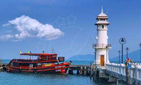 Red wooden ferry boat moored at a concrete pier beside a white lighthouse under blue sky