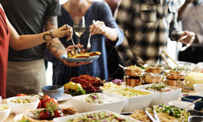 Guests serving themselves from a buffet table laden with salads, breads and dishes at a casual catered meal