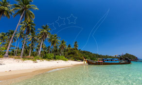 Tropical beach with coconut palms, white sand and long-tail boats moored in clear turquoise shallows under blue sky