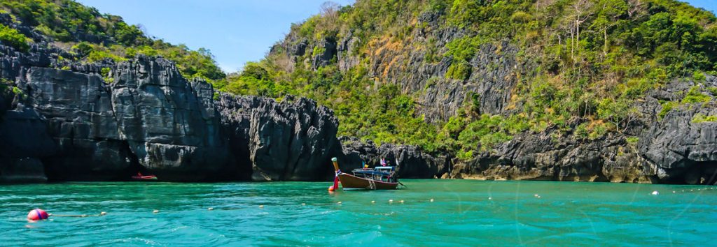Turquoise lagoon surrounded by limestone cliffs with longtail boats and snorkelers