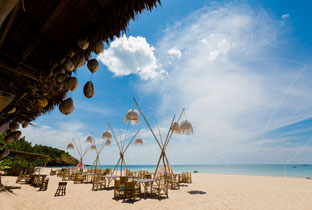 Beachfront restaurant with thatched lanterns, bamboo tables and chairs on white sand beside turquoise sea