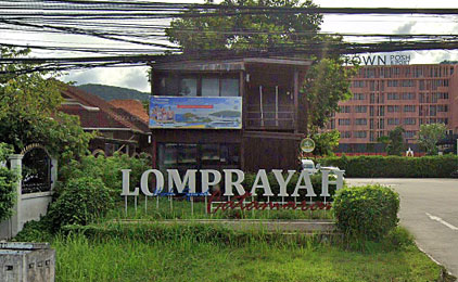 Lomprayah pier entrance sign with overgrown vegetation and urban buildings in background
