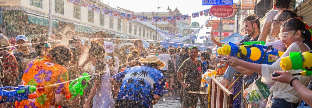 Colorful water fight festival in urban street with crowd throwing colored powder and water balloons