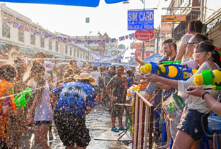 People celebrating with water guns at a crowded festival in an ornate town square during daytime