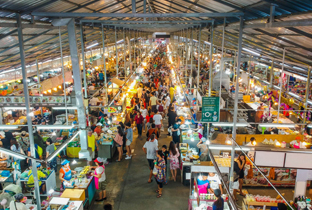 Crowded indoor market with long rows of vendor stalls under metal roof structure