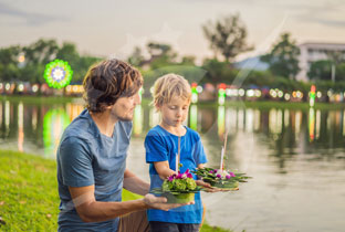 Adult and child releasing seedlings into a waterway beside a grass field with trees
