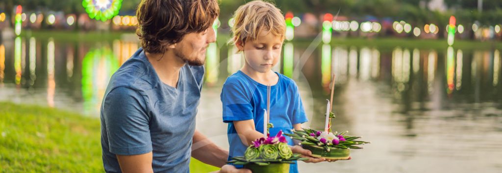 Adult and child releasing flower wreaths into water at a riverside pier at dusk