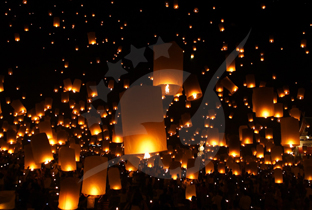Hundreds of glowing orange paper lanterns floating against a black night sky