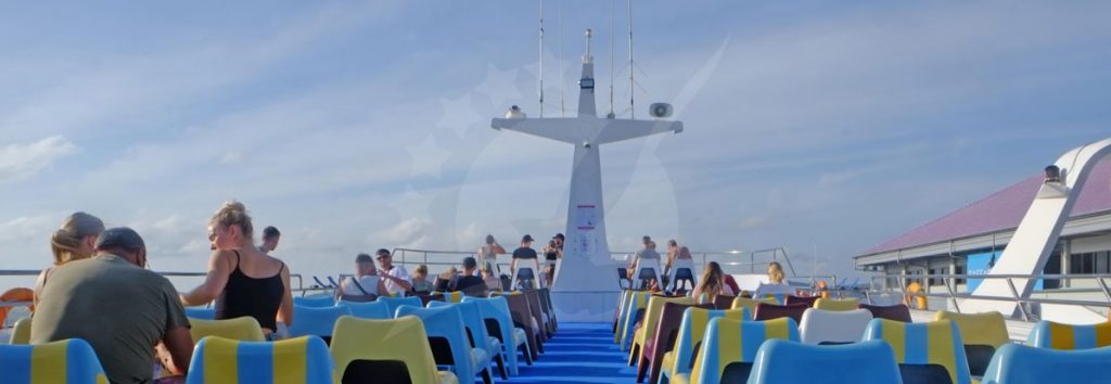 Passengers seated on a ferry with airplane overhead view, blue sea and cloudy sky visible