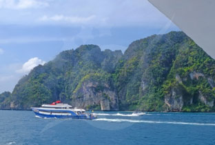 Red and white passenger ferry approaching limestone cliffs and tropical islands in turquoise waters