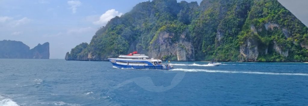 Blue and red ferry boat traveling past limestone cliffs in tropical waters