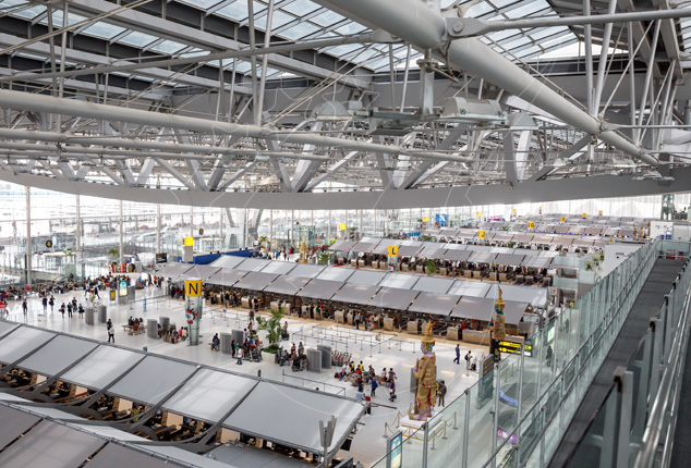 Elevated view of a modern airport terminal check-in hall with rows of counters, glass roof and steel trusses
