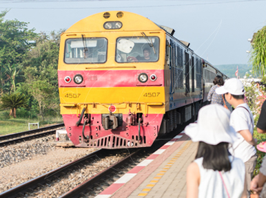 Yellow and red Thai diesel locomotive no. 4507 approaching a station platform as travellers wait beside the track