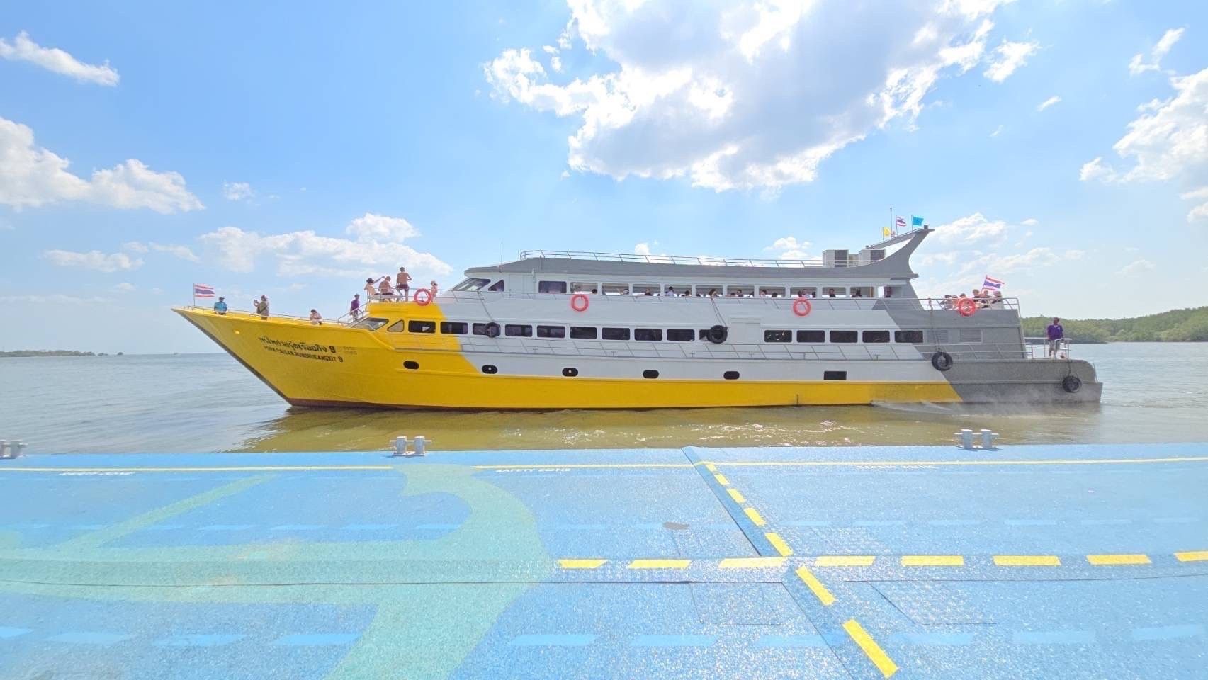 Traghetto passeggeri giallo e bianco con turisti sul ponte si allontana da un molo di cemento blu sotto nuvole luminose