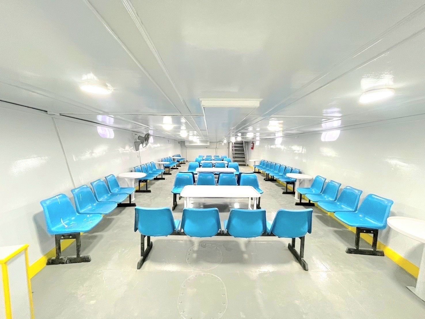 Cabina passeggeri vuota di un traghetto con file di panche blu in plastica, tavoli bianchi e interni bianchi luminosi
