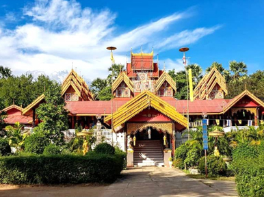 Ornate Thai Buddhist temple with red tiered roofs and gilded gables framed by palms under a blue sky