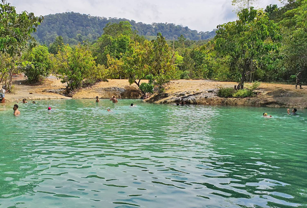 Swimmers in a turquoise natural pool surrounded by jungle-covered hills under an overcast sky