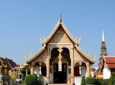 Gilded Lanna-style temple hall with naga staircase and multi-tiered roof beside a golden chedi, Thailand