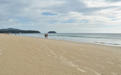 Sandy beach with calm turquoise waters, distant islands, and a few people wading near the shore