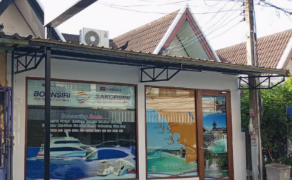 Street-level travel agency storefront with ferry and boat imagery displayed on windows, tropical architecture visible