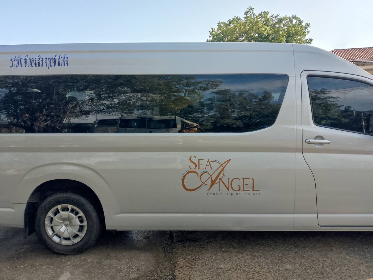 Seite eines weißen Toyota Passagier-Vans mit Logo des Transferunternehmens "Sea Angel" und thailändischer Schrift, im Freien geparkt