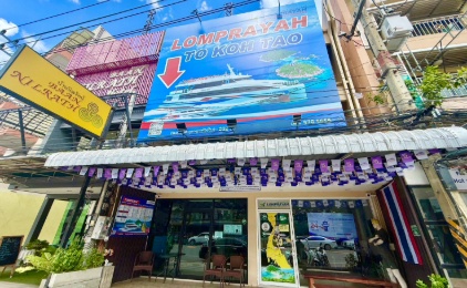 Street-level view of a Thai ferry booking shop with blue signage and purple awning displaying cruise ship imagery