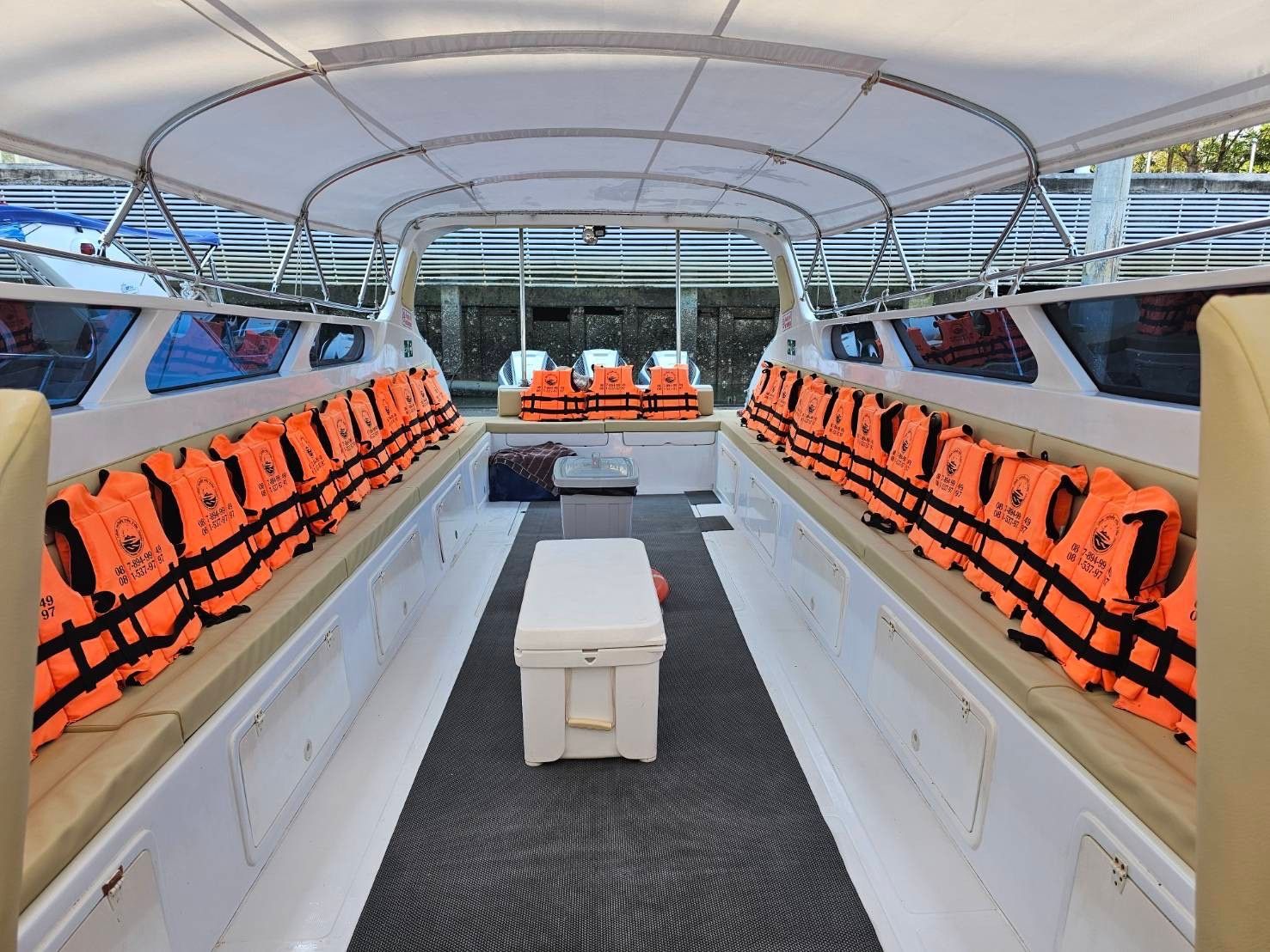 Leeres Passagierdeck eines Speedboots mit orangen Schwimmwesten auf Sitzbänken, weißem Verdeck und Kühlbox