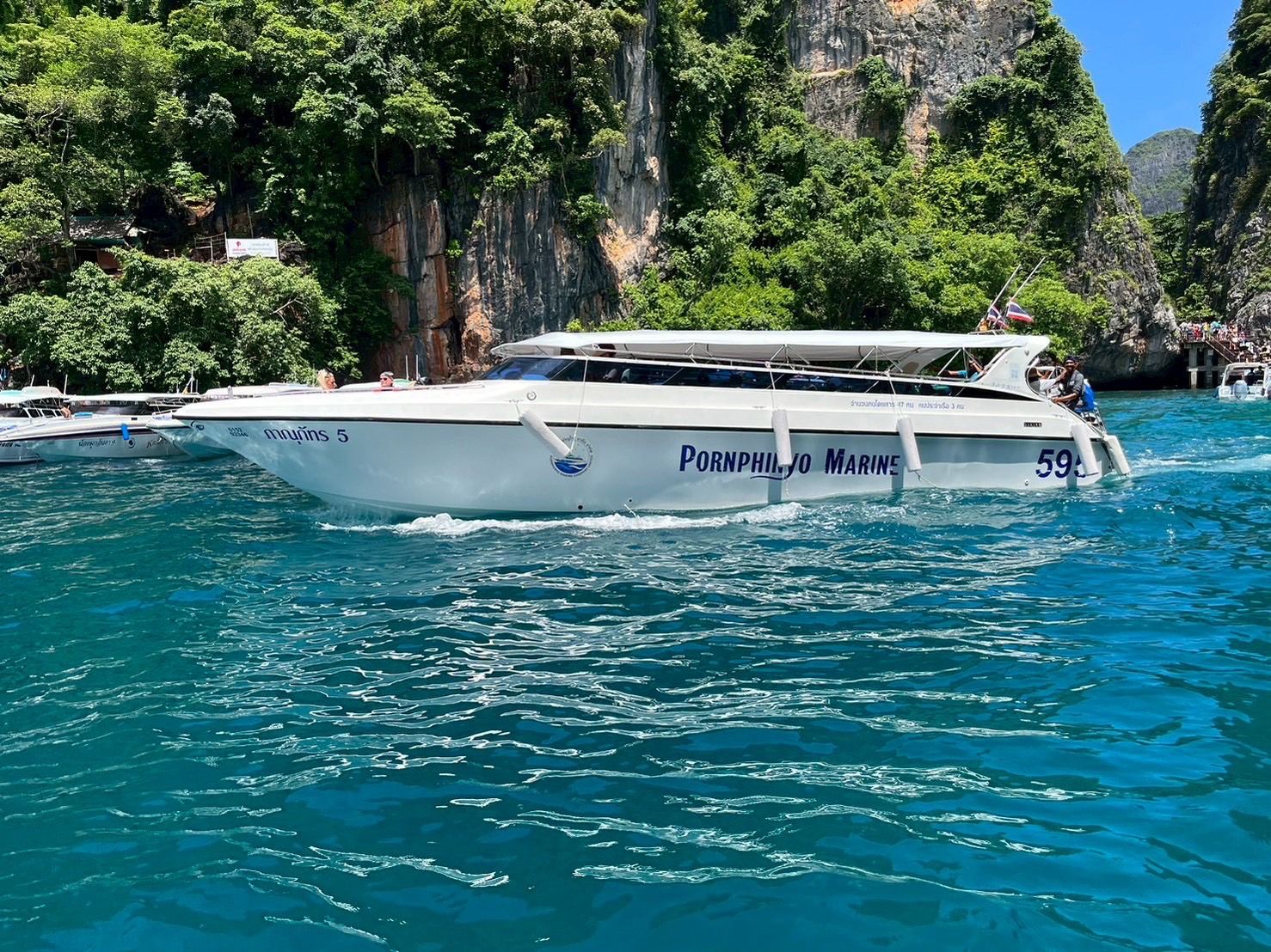 Weißes Touristen-Speedboot mit Sonnenverdeck auf türkisem Wasser unter dschungelbewachsenen Kalksteinfelsen, Thailand