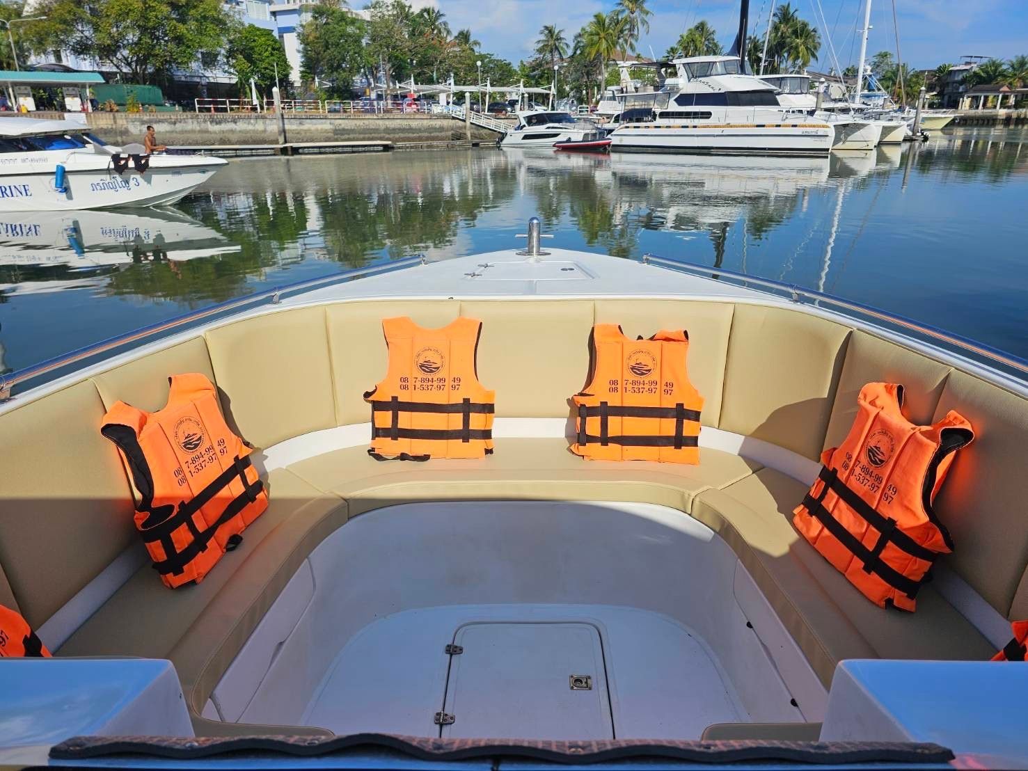 Orangefarbene Schwimmwesten auf cremefarbener Bugsitzbank eines Speedboots im Hafen mit Yachten und Palmen