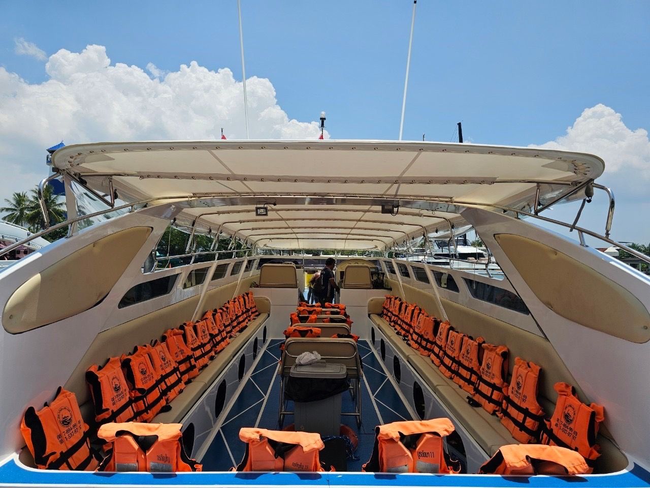 Leeres Speedboot-Passagierdeck mit orangen Rettungswesten auf beigen Sitzbänken unter Sonnendach an thailändischem Pier